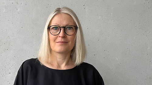 Die Person ist im Porträt vor einer Betonwand zu sehen.