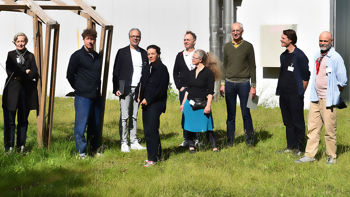 Die 7-köpfige, hochschulunabhängige DIA-Jury 2024 und unsere zwei Organisatoren vor ihrem Rundgang auf der Wiese neben Haus 7.