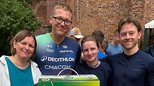 Eine Gruppe von vier Personen steht vor einer Backsteinmauer. Die zwei Frauen und zwei Männer lächelnd in die Kamera. Einer trägt erkennbar ein Fahrradtrikot