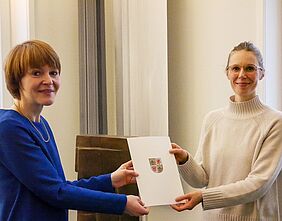 Wissenschaftsstaatssekretärin Susanne Bowen und Professorin  Sophia Martineck halten gemeinsam die Ernennungsurkunde in der Hand.