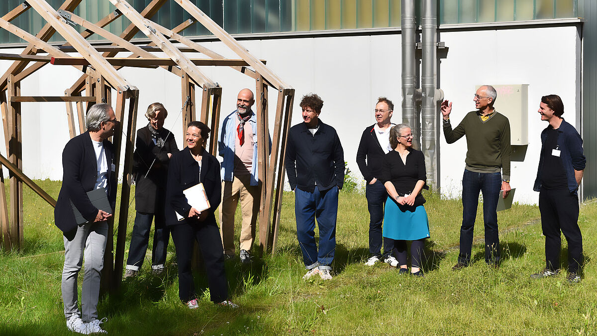 Die 7-köpfige, hochschulunabhängige DIA-Jury 2024 und unsere zwei Organisatoren vor ihrem Rundgang auf der Wiese neben Haus 7.