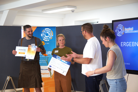 Two winners, Anna-Karina Katt and Karsten Schmiegel, stand with awards and flowers after receiving first place in the external category at the INSPIRED competition.