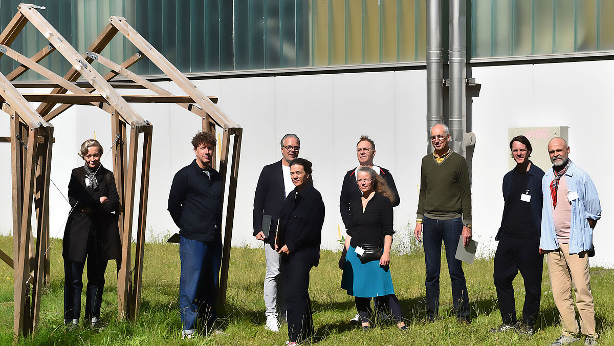Die 7-köpfige, hochschulunabhängige DIA-Jury 2024 und unsere zwei Organisatoren vor ihrem Rundgang auf der Wiese neben Haus 7.