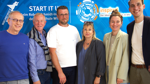 Group photo of six jury members of the INSPIRED competition standing in front of a branded background at Wismar University of Applied Sciences.