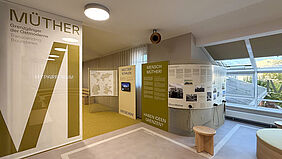 Ausstellungsraum mit Texttafeln und Monitor zur Ausstellung über Müther im Hyparforum, mit Sitzmöbeln und großen Fenstern im Hintergrund.